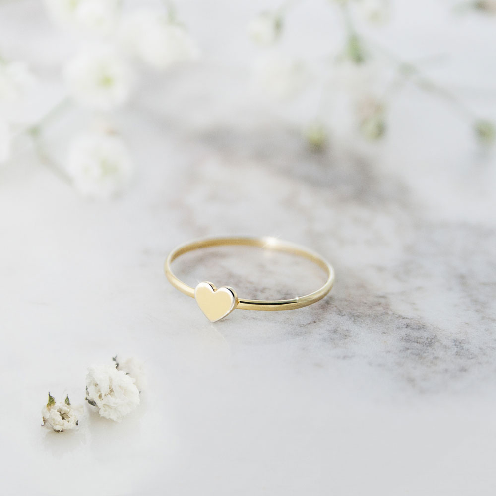 a yellow gold ring with a tiny heart on a grey background with flowers