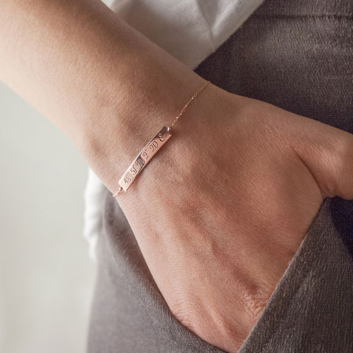 Engraved Coordinates on a Thin Bar Bracelet in Rose Gold Worn By A Woman
