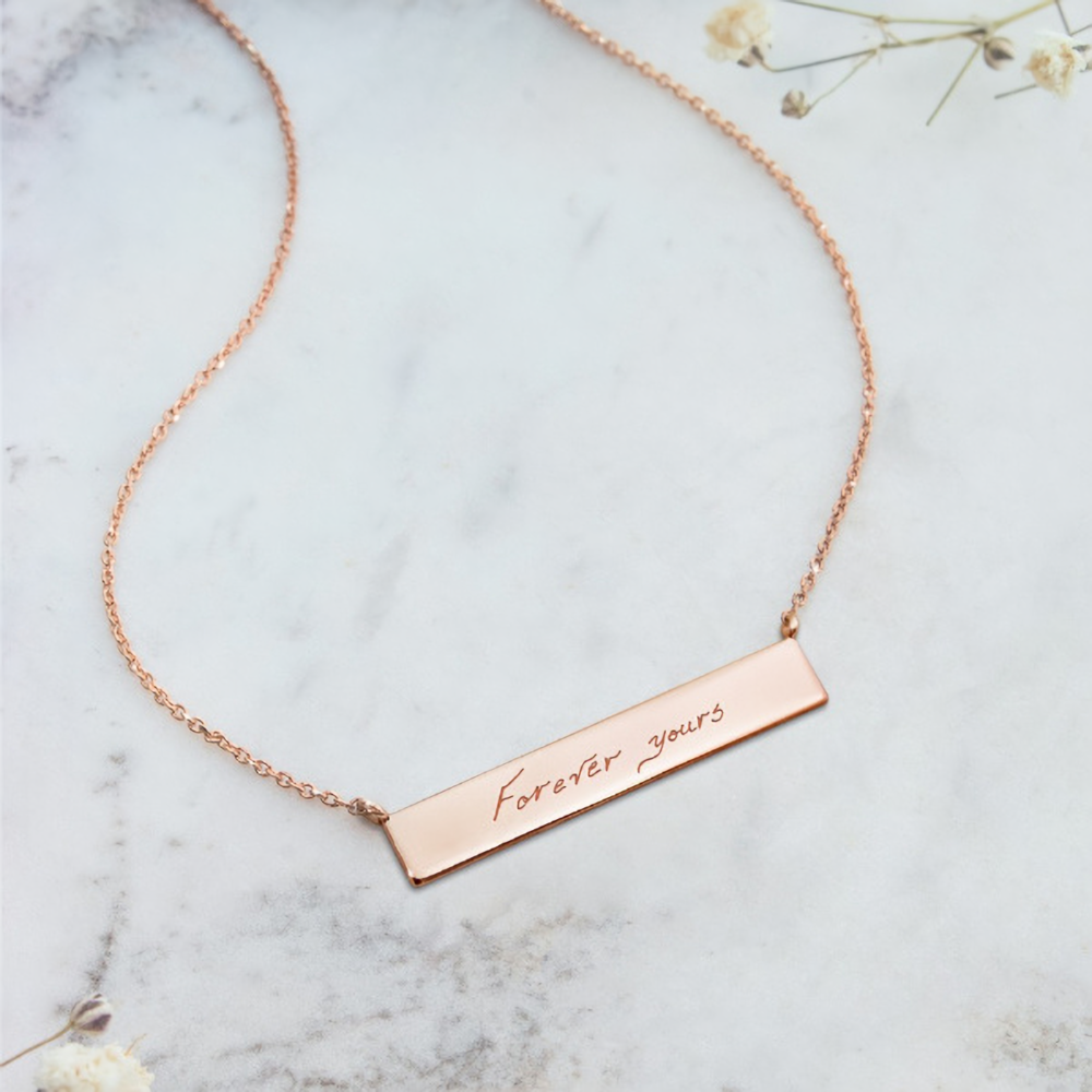 A rose gold bar necklace with a personalized message