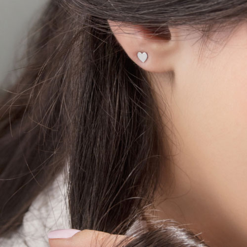Tiny White Gold Heart Studs Worn By A Woman