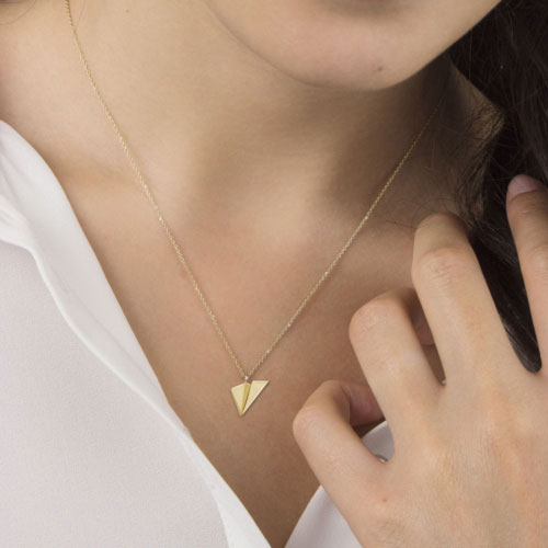 A Two Dimensional Paper Plane Pendant Necklace in Yellow Gold Worn By A Woman