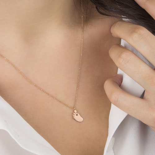 A Small Baby Foot with a Heart Pendant Necklace In Rose Gold Worn By A Woman