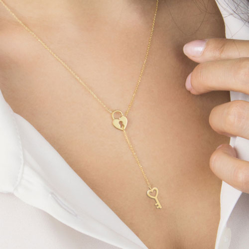 Gold Lariat Style Necklace with a Heart Locket and a Key In Yellow Gold Worn By A Woman
