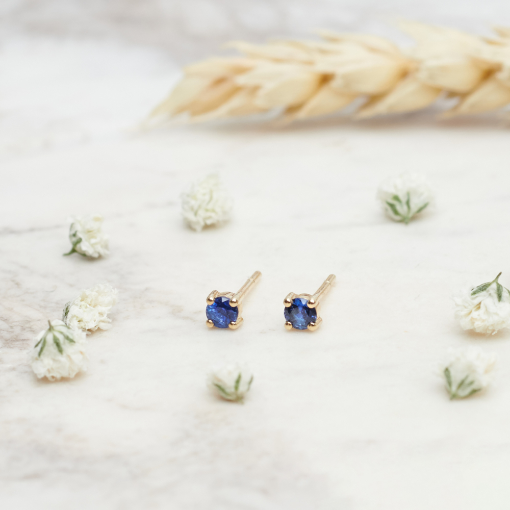 Tiny Royal Blue Sapphire Stud Earrings in Solid Gold with a background with flowers