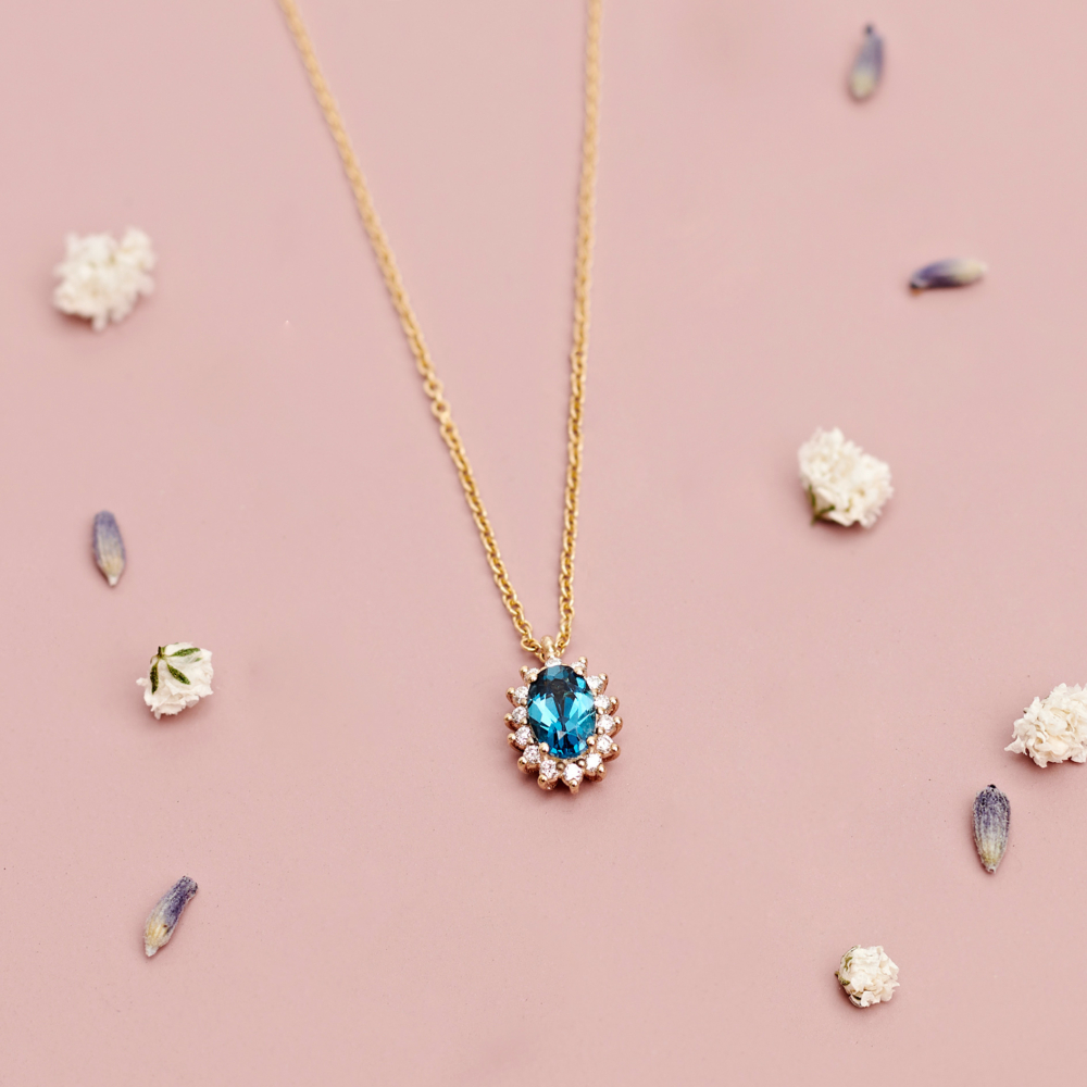 oval London blue topaz with diamonds necklace in gold on a pink background with pedals
