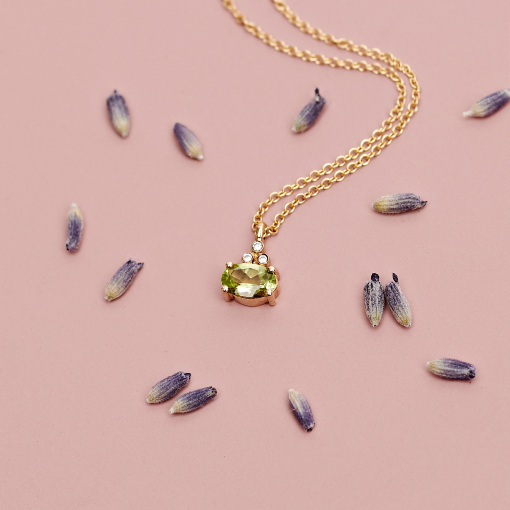 Oval Peridot Pendant with Tiny Diamonds in Solid Gold on a pink background