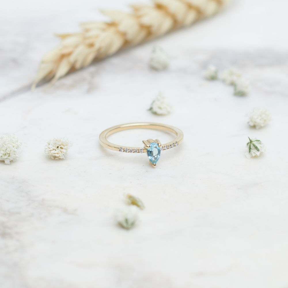 gold ring with swiss blue topaz and tiny white diamonds on a white background with flowers