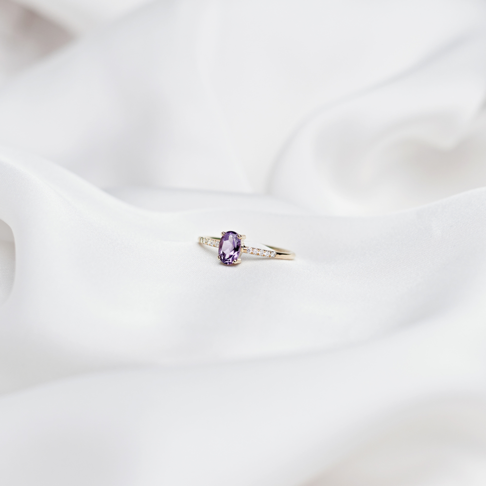 oval amethyst ring with white diamonds in solid gold on a white sheet