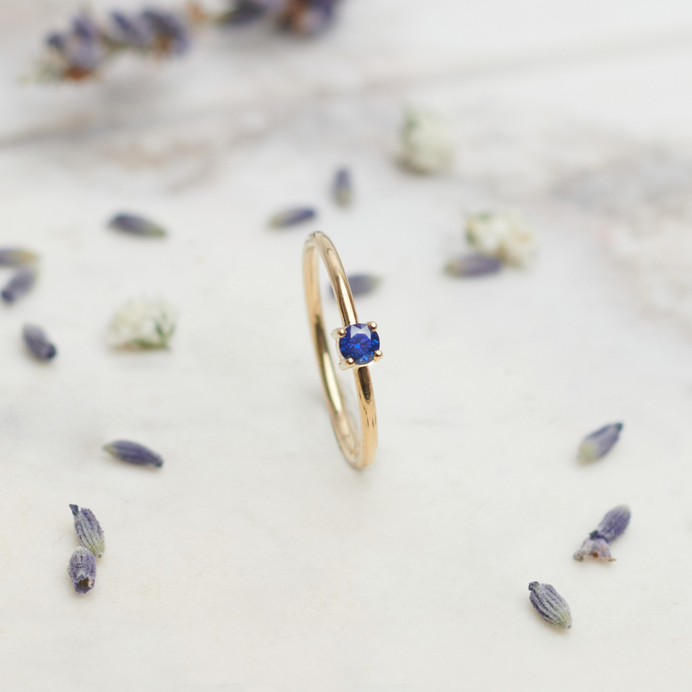 royal blue sapphire ring in solid gold on a grey background with pedals