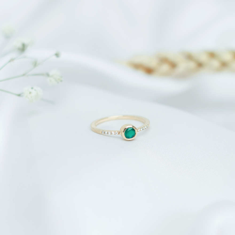A round green agate and white diamond gold ring. on a white sheet