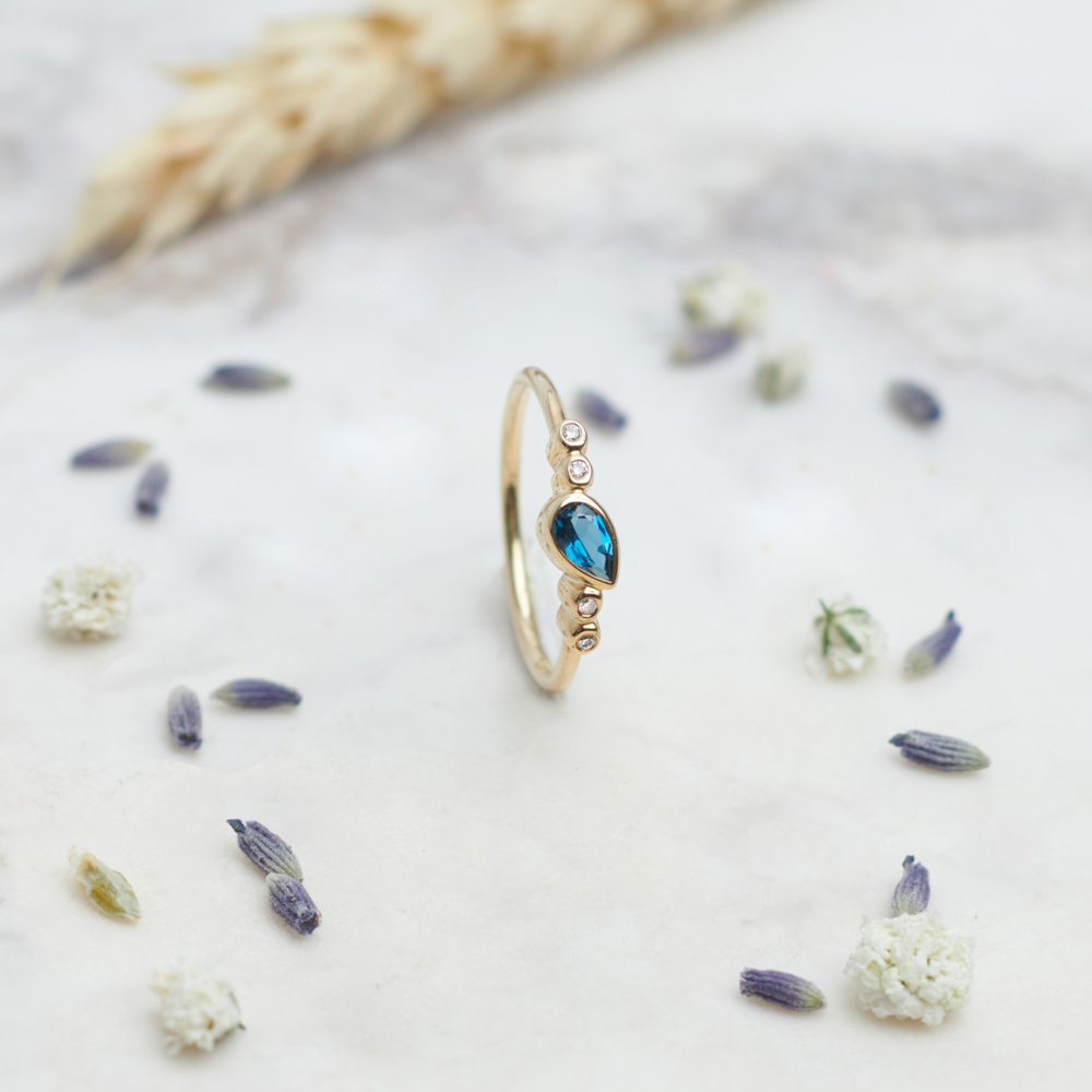 London blue topaz and tiny white diamonds gold ring on a grey background with a flower