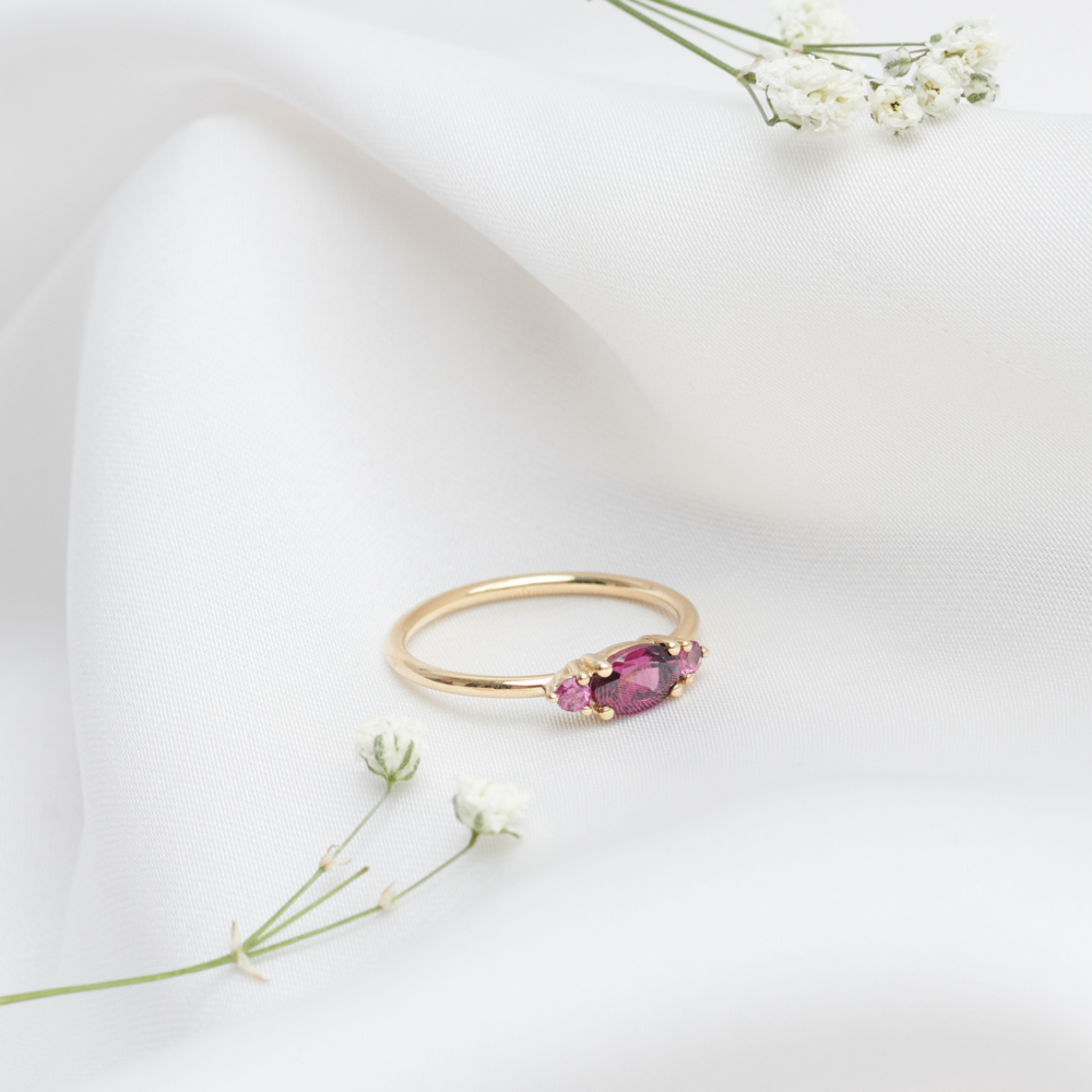 three rhodolite garnet ring in solid gold on a white sheet with flowers