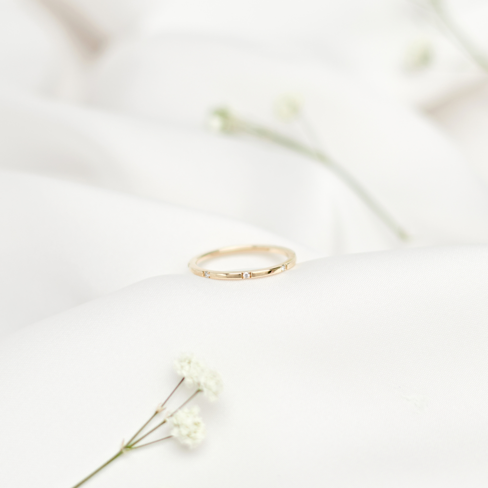 gold band ring with white diamonds on a white sheet with a flower