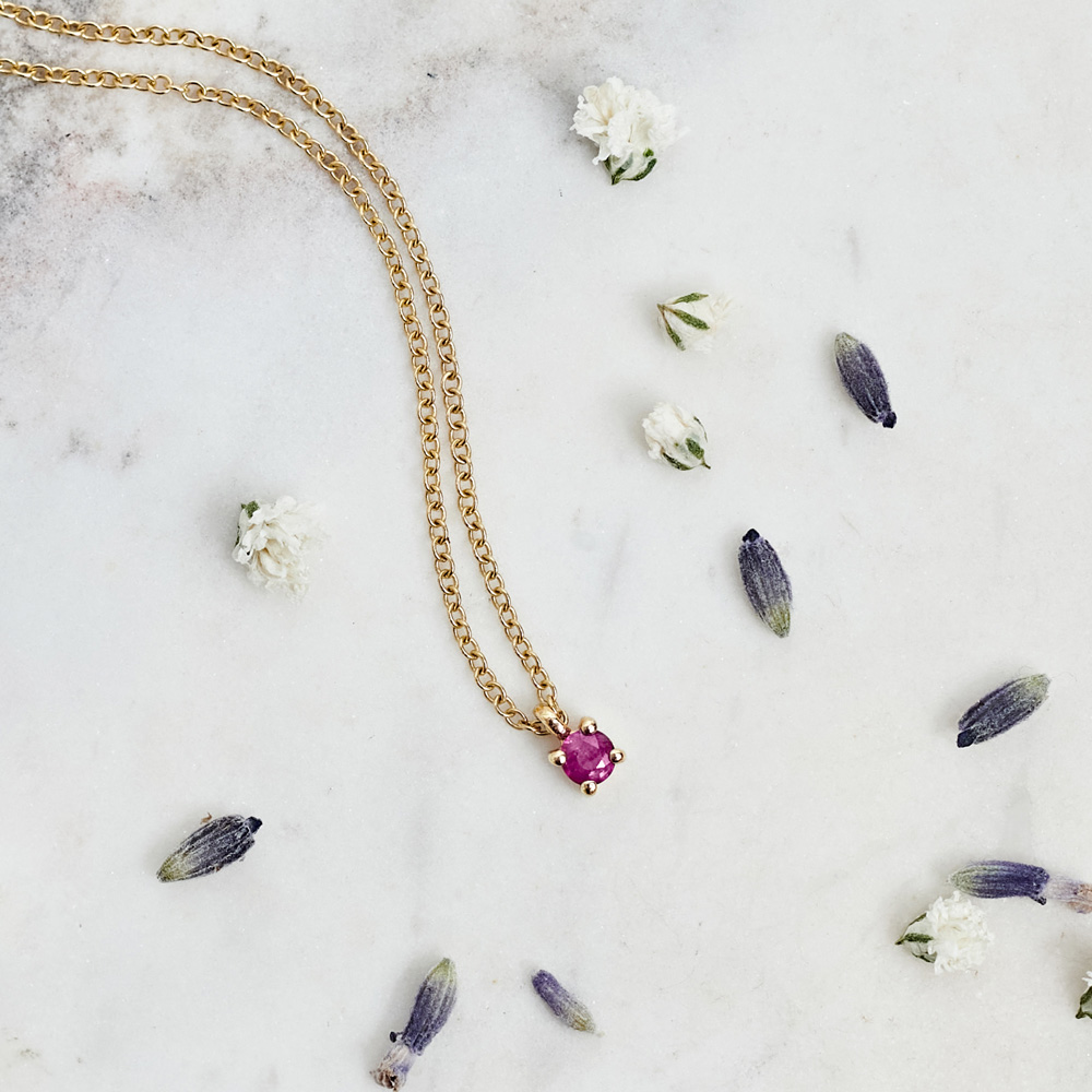 Hot Pink Sapphire Solitaire Necklace in Solid Gold On a grey background with pedals