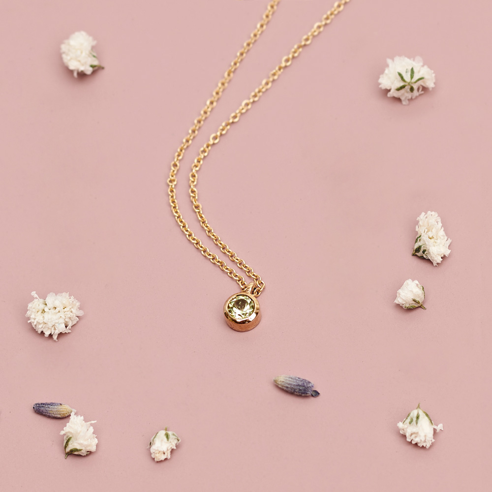 Round Peridot Solitaire Necklace in Solid Gold on a pink background with pedals