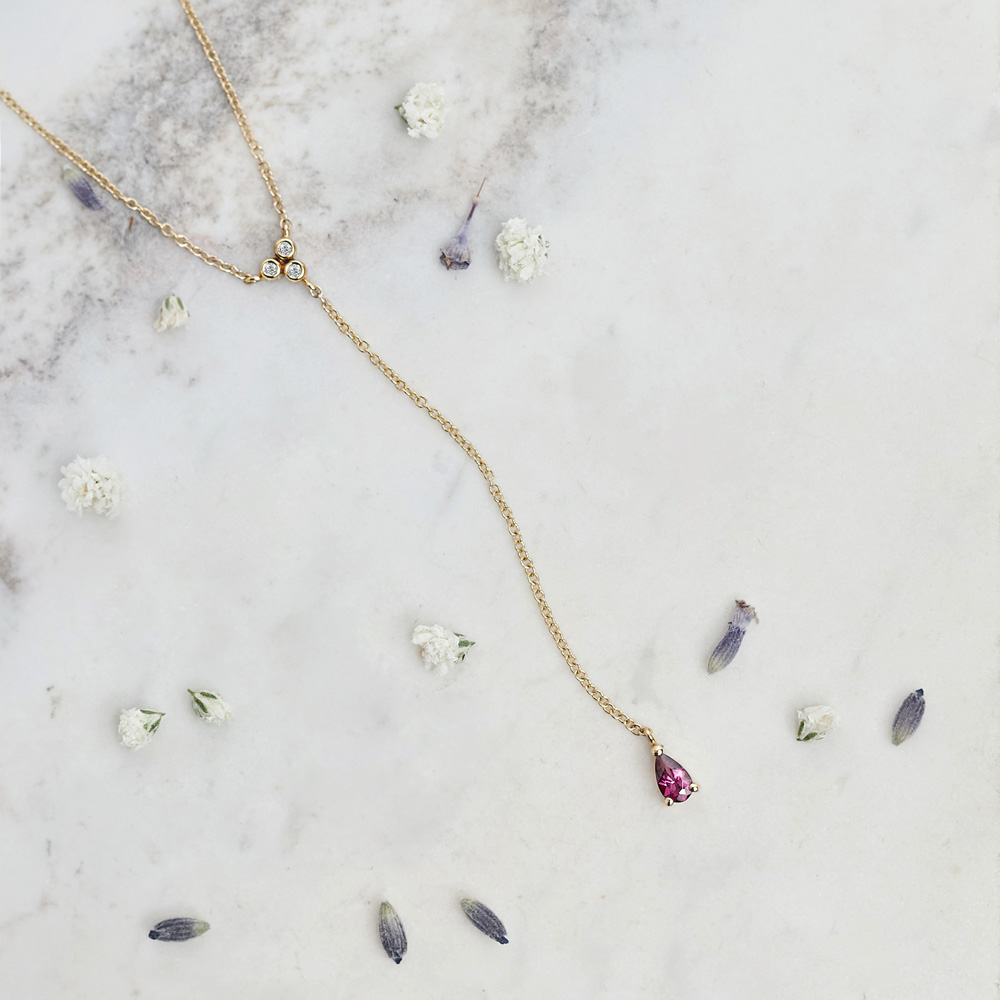 Rhodolite Y Necklace with White Diamonds in Solid Gold on a white background with pedals