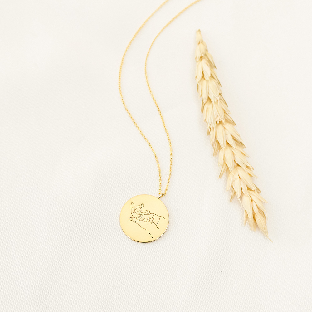 Mother and Baby Hand Gesture Necklace in yellow Gold on a white background a wheat laid next to it